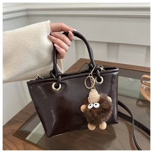 Detail der dunkelbraunen glänzenden Beuteltasche mit FASHION-Prägung und Plüsch-Anhänger
