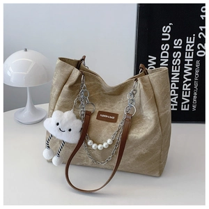 Detail of beige tote bag with metallic chains, pearl strap, and plush cloud charm decor