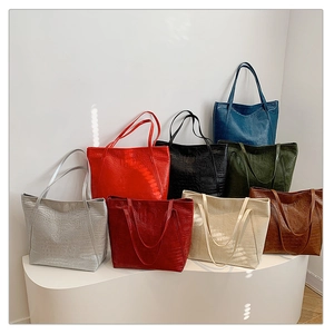 Multiple textured crocodile pattern tote bags in various colors displayed on a white stand
