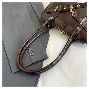 Detail of dark brown glossy patent leather handbag with golden hardware and fashion logo