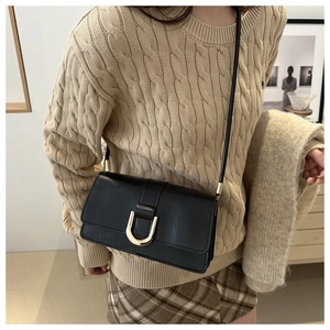 Close-up of black leather crossbody bag featuring a golden U-shaped metallic buckle