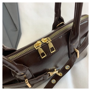 Detail of dark brown glossy leather handbag featuring golden double zippers and fashion stamp