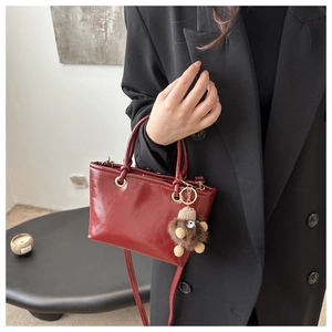Detail of dark red glossy leather handbag with cute plush charm and long strap