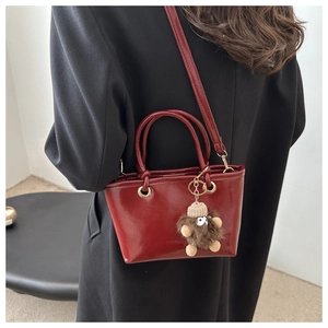 Detail of dark red glossy handbag with plush monster charm on black wool coat