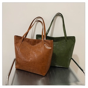 Detail of brown and green crocodile pattern faux leather tote bags on a metal chair