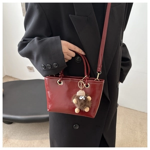 Dunkelrote glänzende Beuteltasche mit Plüsch-Anhänger getragen über schwarzem Blazer