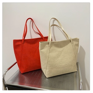 Detail view of large crocodile pattern tote bags in red and beige on a metal rack