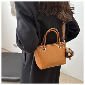 Details der karamellfarbenen Bucket Bag mit goldener Hardware und Plüsch-Anhänger