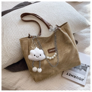 Detail of khaki canvas tote bag with leather handles, pearl chain, and plush cloud charm