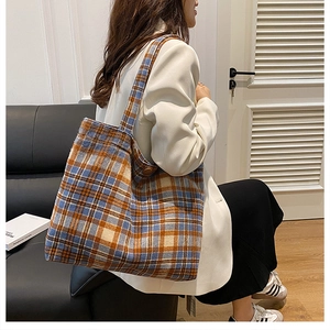 Detail of a large plaid tote bag in wool material shown being worn by a model on a sofa
