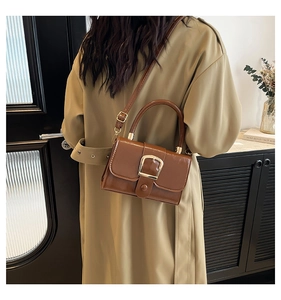 Close-up of retro brown patent leather handbag with a gold buckle worn by a model