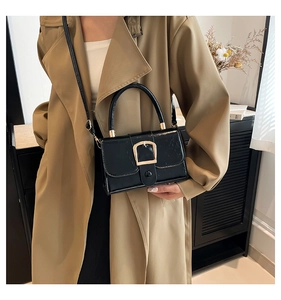 Detail of a black glossy handbag with a gold buckle and slim leather strap