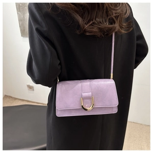 Détail du sac à bandoulière violet lavande avec boucle dorée sur un manteau noir