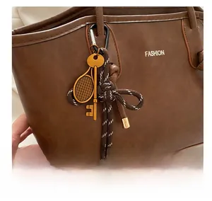 Close-up of golden tennis racket and key keychain on brown leather tote bag