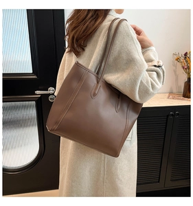 Detail of a brown leather tote bag with vertical stitching and long shoulder straps