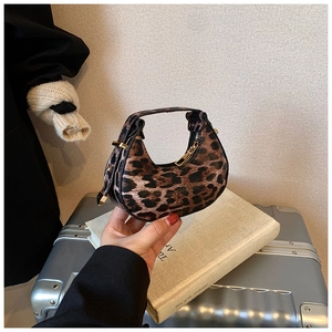 Close-up of leopard print crescent bag with gold zipper on a silver suitcase