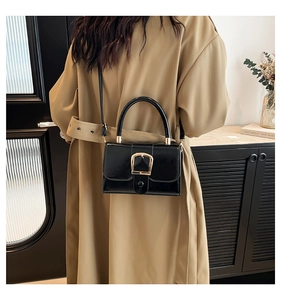 Detailed macro view of black patent leather bag with a large gold horseshoe buckle detail