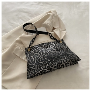 Detail van luipaardprint enveloptas met zwarte ketting en gouden hardware op blazer