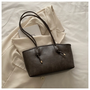 Detail of dark brown leather tote bag with knot straps on cream blazer background