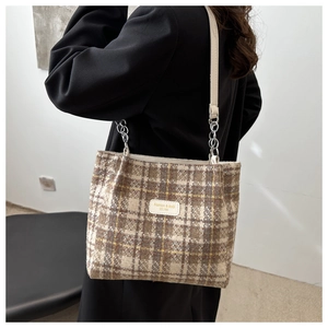 Gros plan d'un sac cabas à carreaux marron avec écusson en cuir et bandoulière en chaîne