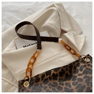 Detail van luipaardprint handtas met amberen acryl ketting op een beige blazer