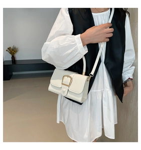 Detail of white faux leather crossbody bag with gold U-shaped buckle and slim strap