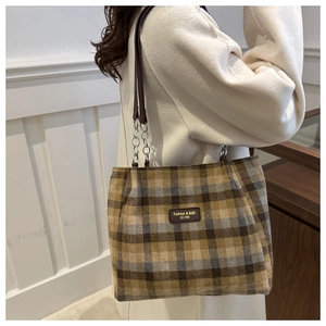 Detail of plaid wool tote bag with chain strap and leather logo patch on shoulder