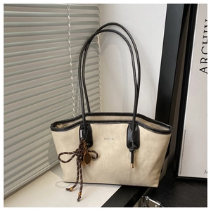 Detail of beige tote bag with black trim and unique metal tennis racket charm hanging on strap