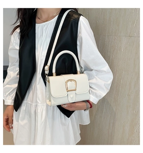 Close-up of a white leather crossbody bag with a gold horseshoe buckle on a model