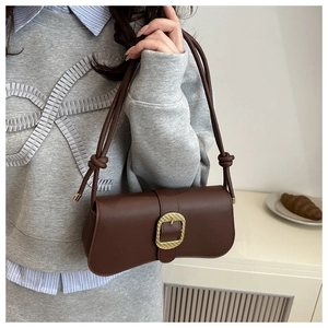 Détail d'un sac sous le bras en cuir marron vintage avec boucle dorée et bandoulière nouée