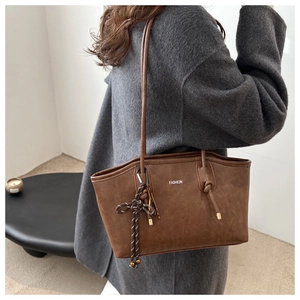Close-up of brown textured tote bag with Fashion text and braided knot charm detail