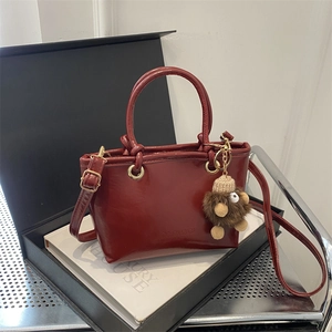 Schicke weinrote Leder-Eimertasche mit Goldbeschlägen und Plüschmonster-Anhänger