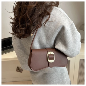 Détail d'un sac baguette marron foncé avec boucle dorée porté à l'épaule par un mannequin