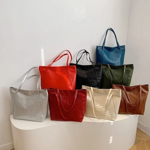 Large crocodile embossed tote bags in eight solid colors on a white minimalist display stand