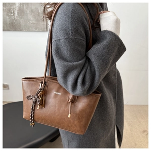 Close-up of vintage brown tote bag with FASHION logo and unique woven knot pendant detail
