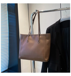 Detailed view of brown leather tote bag hanging against a professional dark suit background