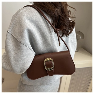 Detail of dark brown leather baguette bag featuring a textured gold metal buckle and strap
