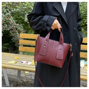 Detail of burgundy lychee leather handbag with white contrast stitching and gold rivets