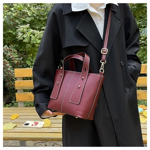 Close-up of wine red lychee grain leather handbag with gold studs in an outdoor autumn setting