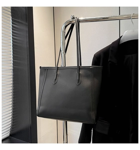 Detail of a black large tote bag with matte leather finish showing stitching and dual straps