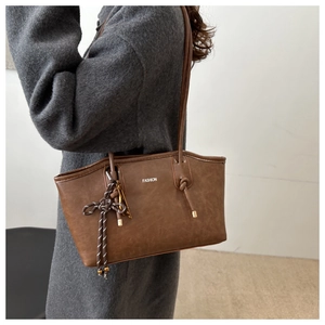 Close-up of brown leather tote bag detail with decorative knots and fashion logo