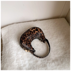 Detail view of leopard print crescent bag on white faux fur background with gold zipper