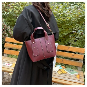 Detail of burgundy leather handbag with litchi texture and gold studs in outdoor setting