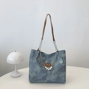 Blue denim tote bag with leather handles and pearl chain on a clean white display stand
