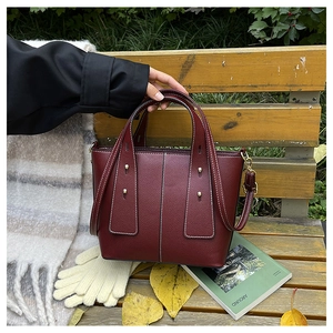 Close-up of burgundy lychee leather handbag with gold studs on a wooden bench