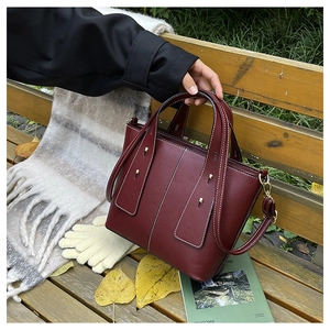 Macro detail of wine red litchi grain leather bag with contrast stitching and golden rivets