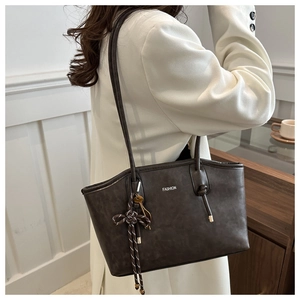 Detail of dark brown leather tote bag with woven bow charm and fashion lettering