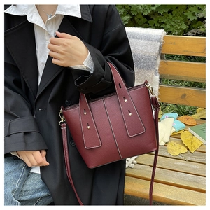 Outdoor view of a wine red pebbled leather handbag with gold studs and a wide strap