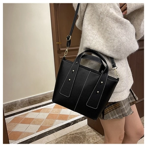 Detail of black pebbled leather tote with white stitching and gold hardware on a model