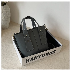 Detailed view of gray lychee texture tote bag with gold hardware in branded packaging box